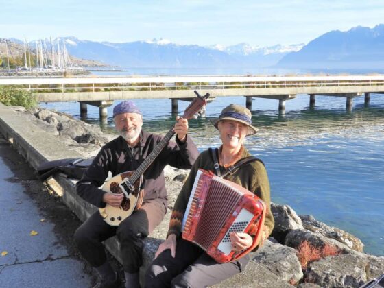 Deux personnes assises sur un banc au bord d'un lac avec un accordéon dans la montagne