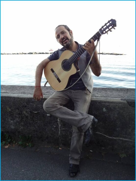 Un homme tenant une guitare acoustique devant un plan d’eau.