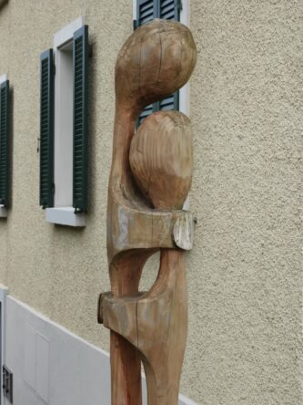 Une sculpture en bois représentant un couple devant un immeuble.