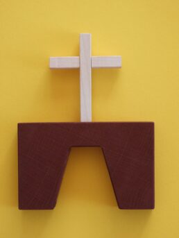 Une croix en bois au sommet d’un mur jaune.