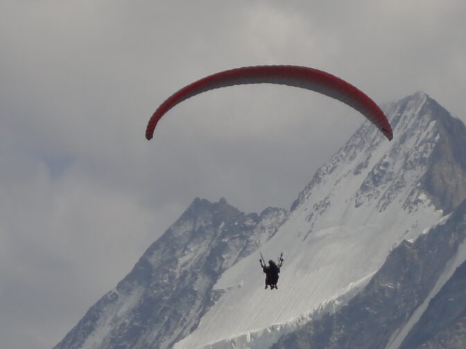 Une personne en parapente au-dessus d'une montagne enneigée, capturant l'essence de L'ami et l'oisillon.