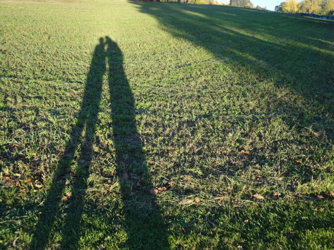 L'ombre de deux personnes sur un terrain herbeux, symbolisant l'amitié et la nature.
