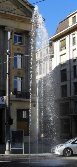 Une voiture roulant dans une rue avec une fontaine devant elle.