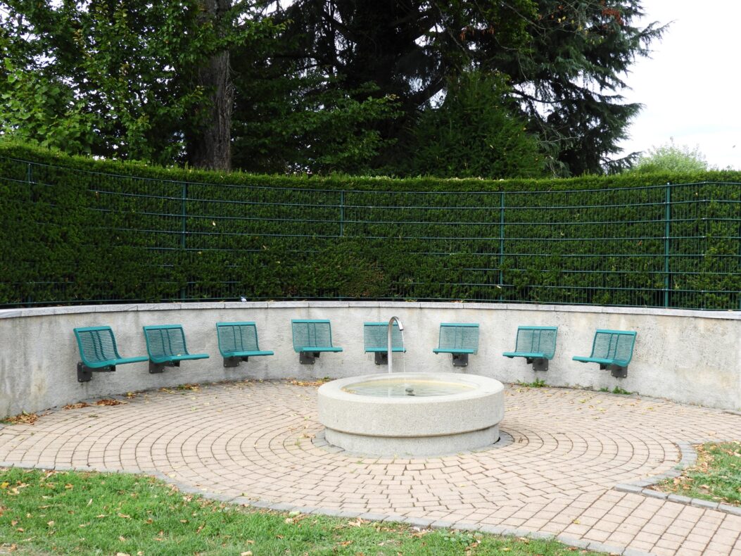 Un groupe de bancs verts en cercle autour d’une fontaine.