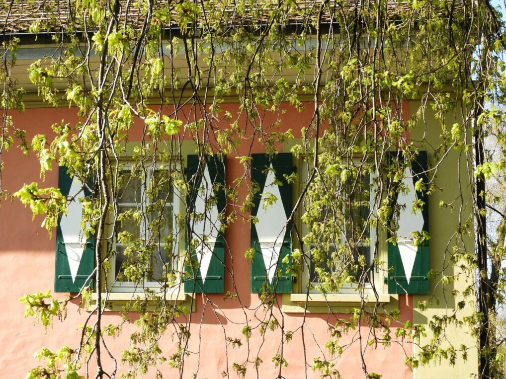 Une maison rose aux volets verts.