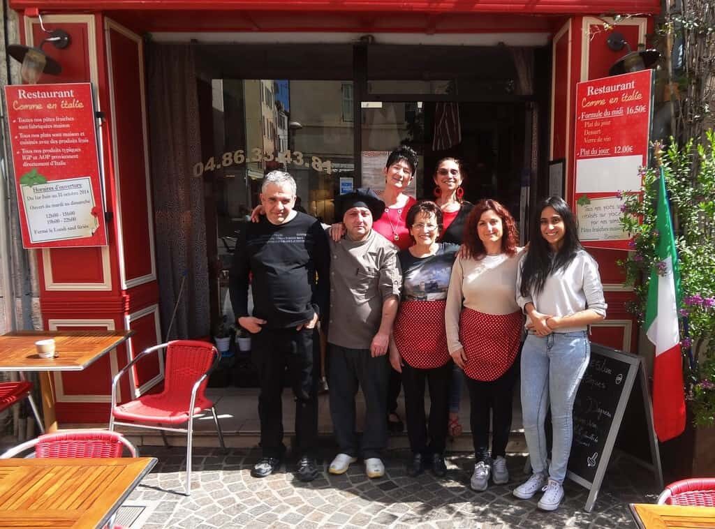 Un groupe de personnes posant devant un restaurant Comme en Italie.