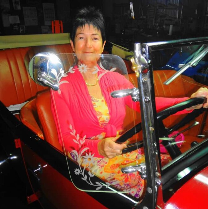 Une femme assise sur le siège conducteur d’une voiture ancienne.