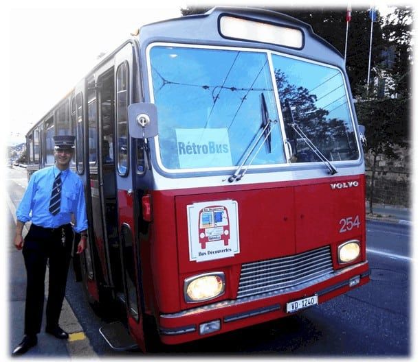 Un homme debout à côté d’un bus rouge et blanc.